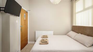 A bedroom with a bed, a wooden door, a white radiator, and a window with blinds.