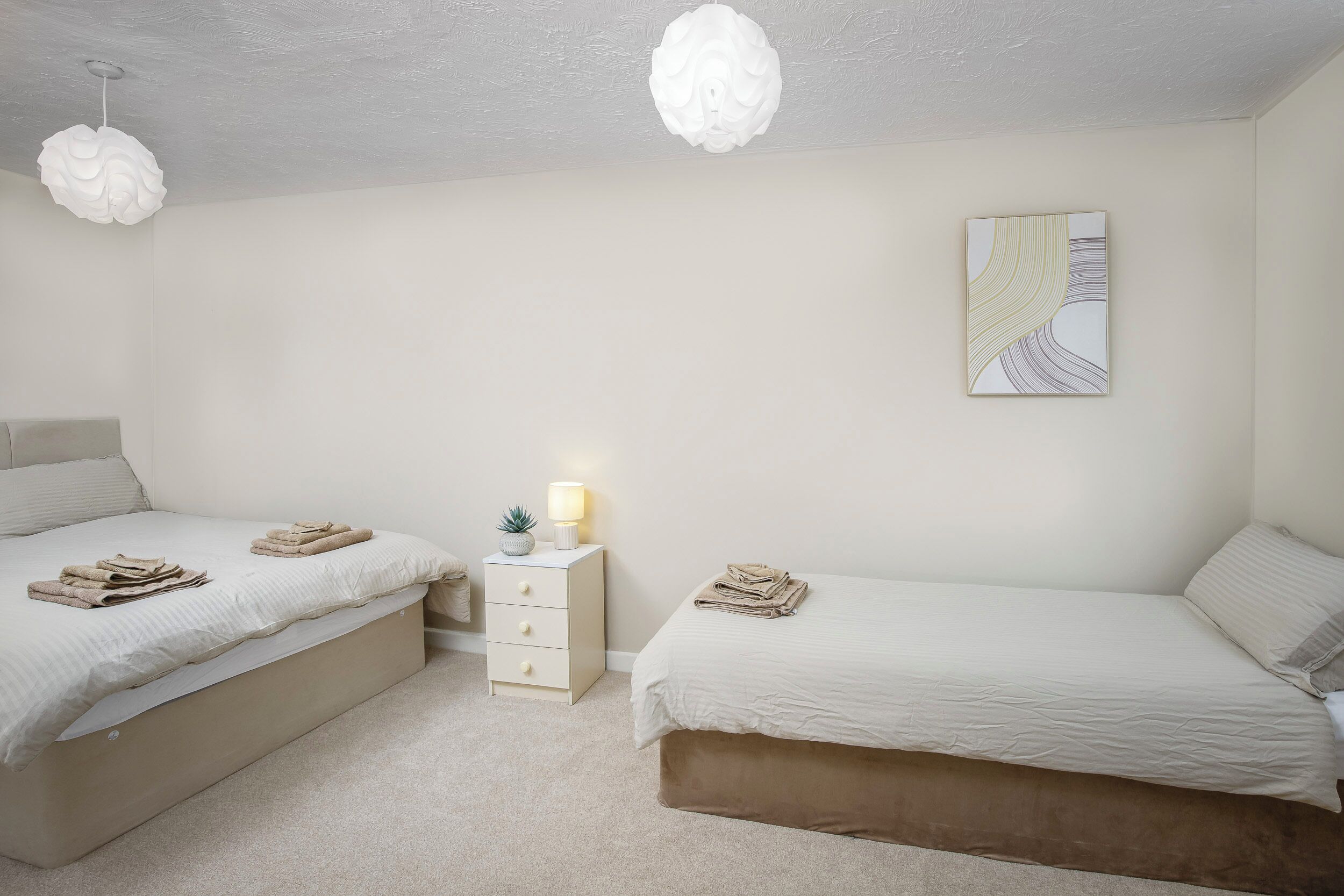 A bedroom with two beds, a bedside table with a lamp, and a wall-mounted artwork.