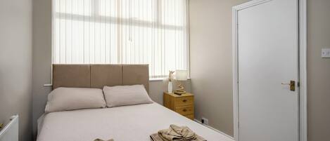 A neatly made bed with a headboard, a bedside table with a lamp, and a door to the right.