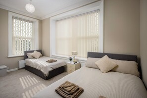 A bedroom with two beds, a nightstand, a lamp, and a radiator. - Hotel Sofia (Blackpool)