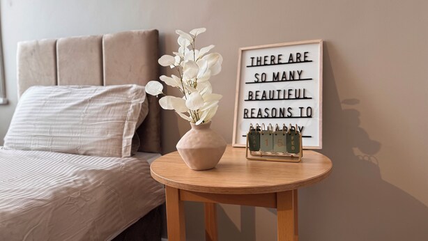 A bedroom with a bed, a bedside table with a vase of flowers, a framed inspirational quote, and a calendar. - Hotel Sofia (Blackpool)
