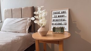 A bedroom with a bed, a bedside table with a vase of flowers, a framed inspirational quote, and a calendar. - Hotel Sofia (Blackpool)