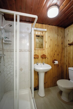 A bathroom with wooden walls, a white sink, a toilet, and a glass-enclosed shower. - Hotel Sofia (Blackpool)