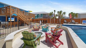 Un área de piscina con sillas Adirondack, una terraza de madera y un pequeño hogar para fuego.