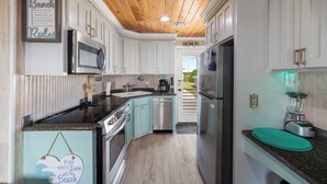 Una cocina con armarios blancos, techo de madera, electrodomésticos de acero inoxidable y encimera verde azulado.