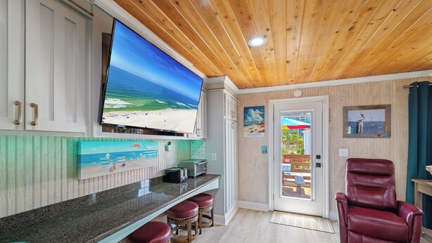 Una cocina con un televisor grande, techo de madera y vista al mar a través de la puerta.