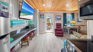 Una cocina con televisor, techo de madera y un comedor con una silla roja.