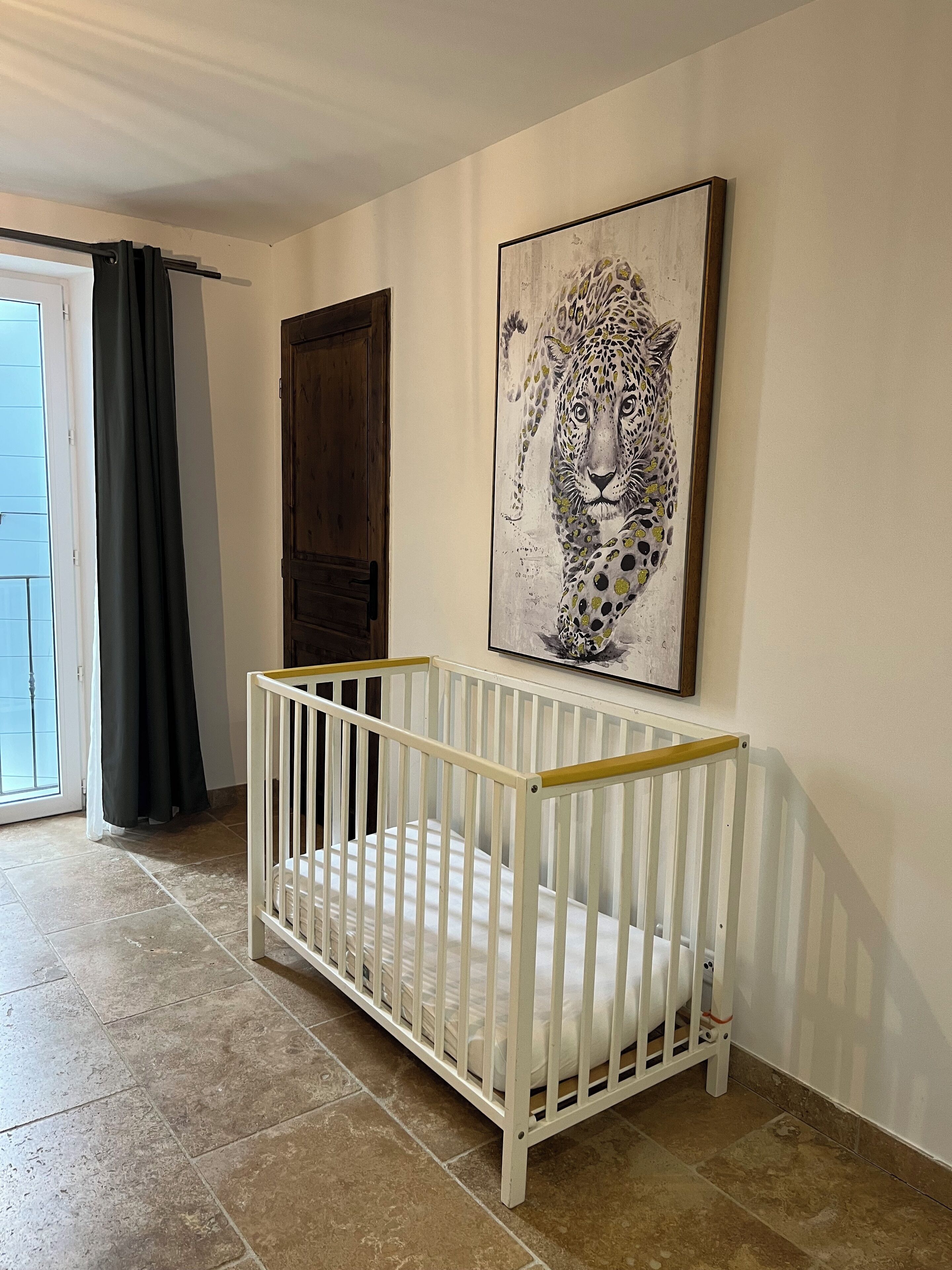 A room with a white crib, a door, and a large leopard painting on the wall.