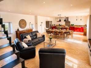 A spacious living area with a black leather sofa, a dining table set for six, and a kitchen in the background with red cabinets. - MAS DE LA BERRE: SOUTHERN DROME AND GATEWAY TO THE ARDÈCHE, VAUCLUSE, AND GARD (Donzère)
