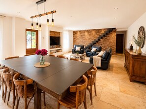 A spacious living area with a dark wooden dining table, comfortable seating, a brick accent wall, and a staircase leading to another level. - MAS DE LA BERRE: SOUTHERN DROME AND GATEWAY TO THE ARDÈCHE, VAUCLUSE, AND GARD (Donzère)