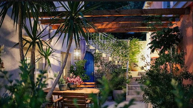 Un espace extérieur aménagé en terrasse, avec une table et des chaises en bois, entouré de plantes en pot et agrémenté d’une structure en forme de pergola.