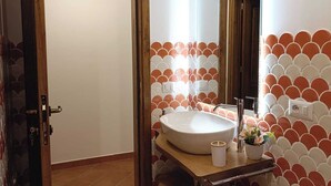 A bathroom with a wooden door, a white sink with a mirror above it, and a tiled wall with a scalloped pattern. - Apartment in the heart of the Amalfi Coast (Praiano)