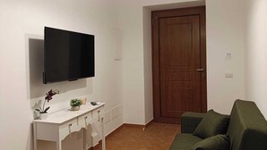 A living room with a flat-screen TV, a white console table, a green sofa, and a wooden door. - Apartment in the heart of the Amalfi Coast (Praiano)