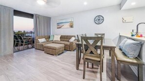 Un salon moderne avec un canapé d’angle, une table à manger avec des chaises, un ventilateur de plafond et une vue sur l’extérieur.