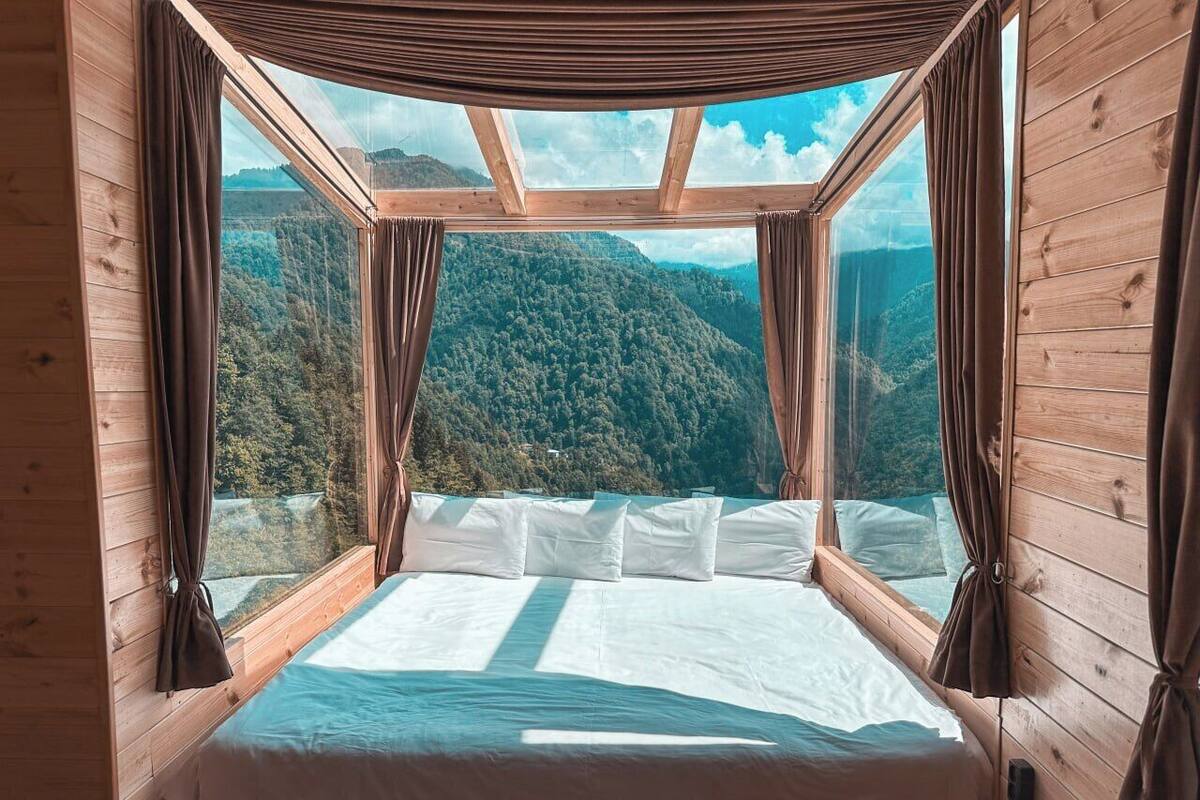 A bedroom with a bed, curtains, and a view of a forested mountain.