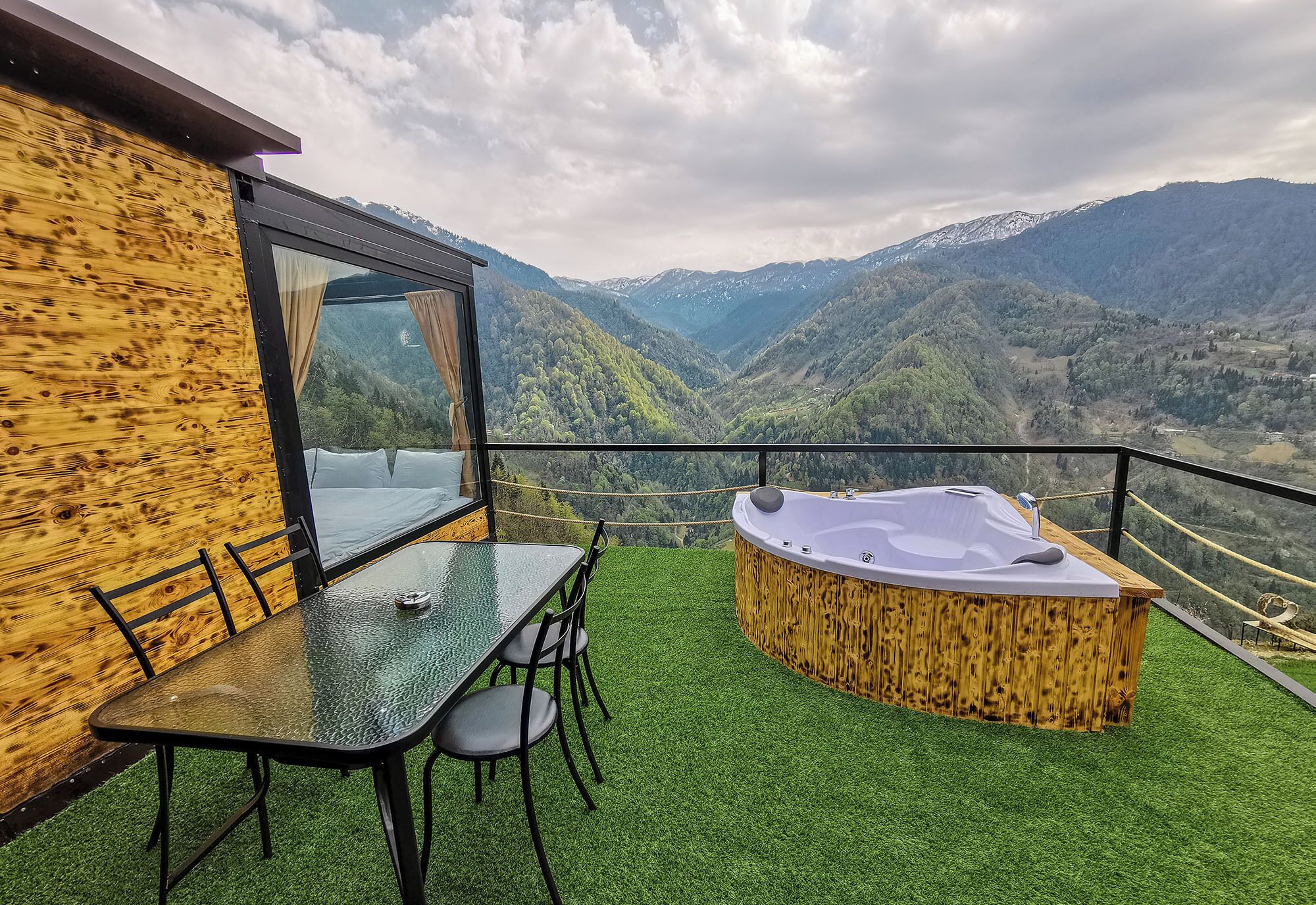 A balcony with a table and chairs, a hot tub, and a view of mountains.