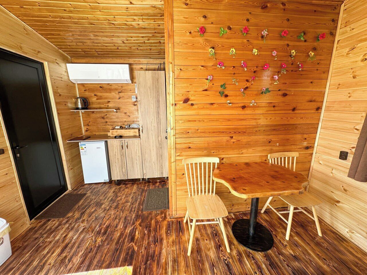 A wooden interior with a dining area, a small kitchenette, and a door.