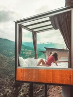 Una cama con estructura de madera y ropa de cama blanca, con un paisaje montañoso de fondo.