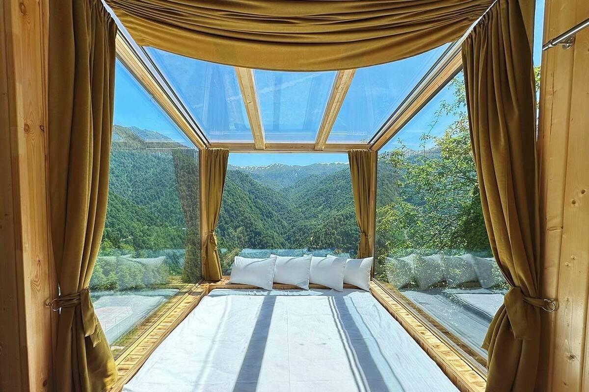 A bed with a view of a mountainous landscape through a skylight.