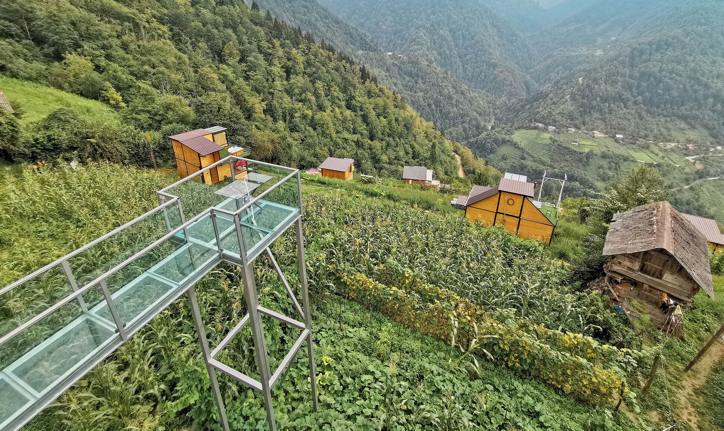 A rural landscape with a glass bridge and several wooden houses.