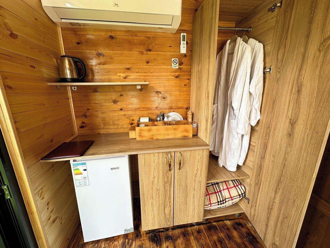 Een compacte kitchenette met een inbouwkoelkast, houten kastjes, een spoelbak en een ophangrek.