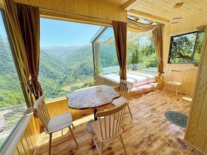 Une cabane en bois avec une table ronde, deux chaises, un lit et de grandes fenêtres donnant sur une vue imprenable sur les montagnes.