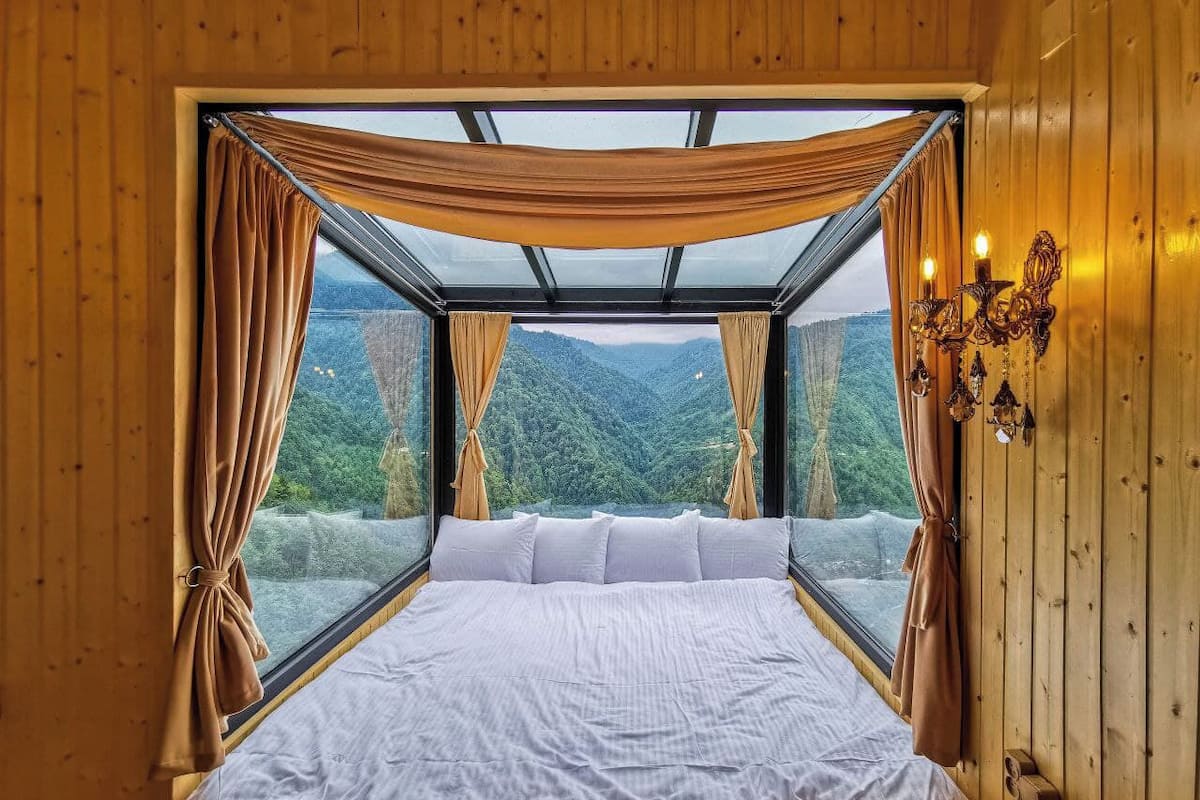 A bedroom with a large bed, wooden walls, and a view of a forest through a glass ceiling.