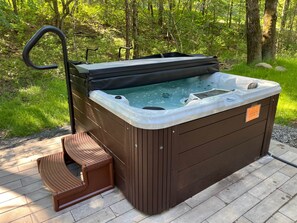 Un jacuzzi con cubierta de madera y un banco, rodeado de follaje.