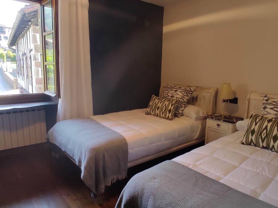 A hotel room with two beds, a desk, a window with curtains, and a view of the street outside.