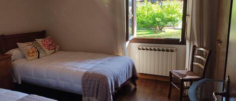 Ein Schlafzimmer mit einem Bett, einem Sessel, einer Heizung und einem Fenster mit Blick auf Grünflächen.
