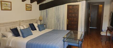 A bedroom with a bed, a glass table, a wooden door, and a chair.