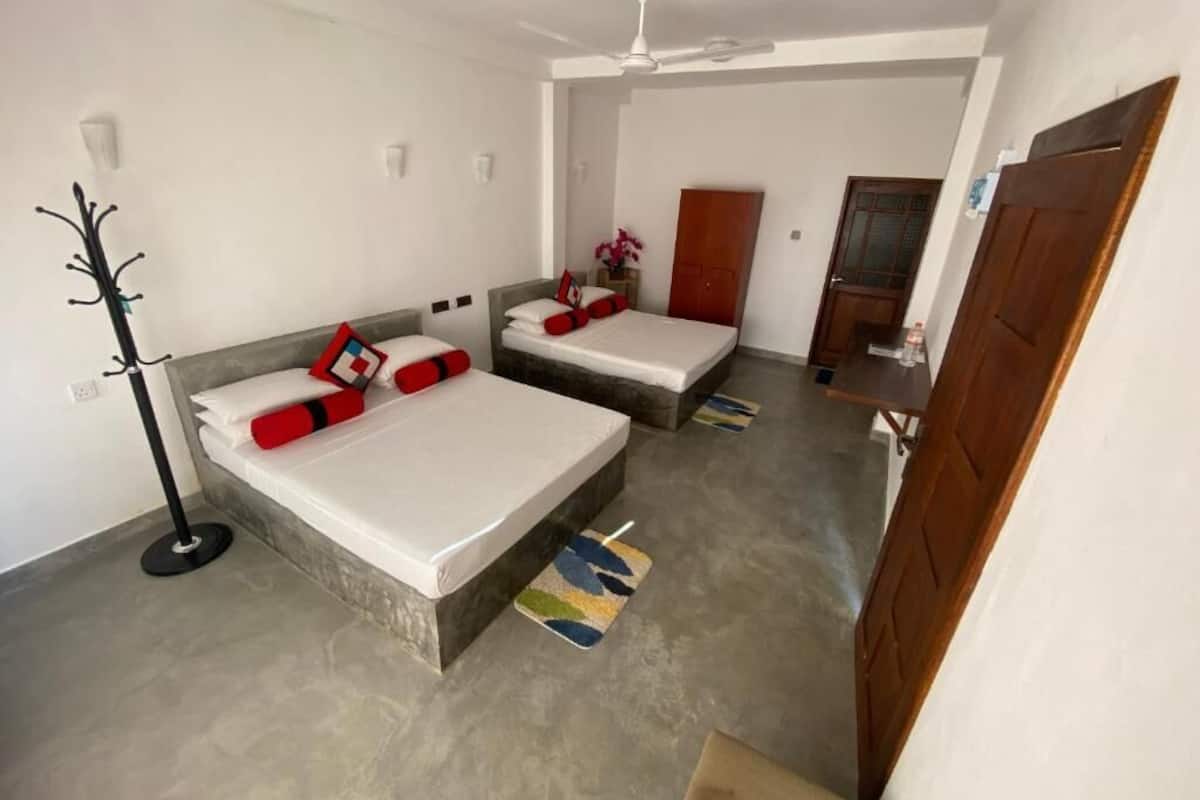 A bedroom with two beds, a ceiling fan, a coat rack, and a door.