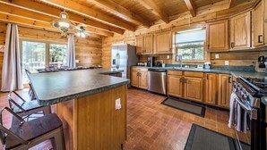 A spacious kitchen with wooden cabinets, a large island, stainless steel appliances, and a view of the outdoors.