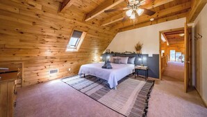 A cozy bedroom with a wooden ceiling, a bed, a nightstand, and a window.