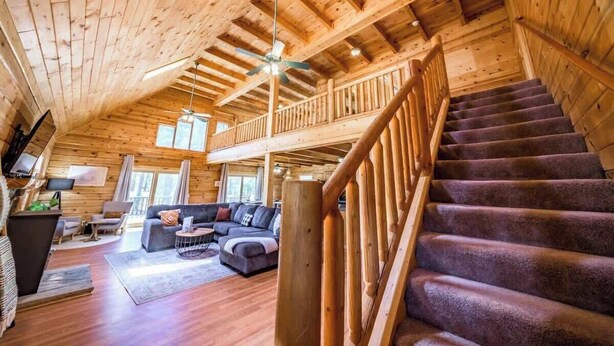 A spacious wooden cabin with a loft bedroom, a cozy living area with a sofa and TV, and a staircase leading to the upper level.