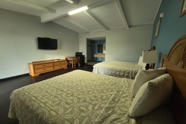 Habitación de hotel con dos camas, un escritorio, televisión y baño visible a través de una puerta abierta.