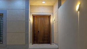 A wooden door with a metal handle, flanked by two wall-mounted lights, leading to a tiled entrance area. - Al-Jamwaut B - Nozol Noor 7 (Madinah)