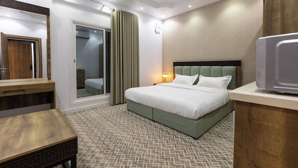 A modern hotel room with a large bed, a wooden desk, a mirror, and a view of the outside. - Al-Jamwaut B - Nozol Noor 7 (Madinah)