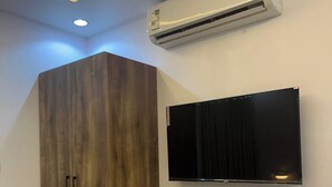 A room with a wooden wardrobe, a mounted flat-screen TV, and an air conditioning unit. - Al-Jamwaut B - Nozol Noor 7 (Madinah)