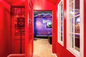Un couloir aux murs rouges, décoré sur le thème de Harry Potter, avec un vieux téléphone à cadran et un fauteuil en cuir.