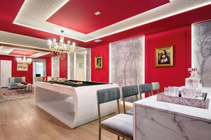 Une table de billard au design moderne, un lustre et un mur d’accent rouge agrémenté d’une œuvre d’art encadrée.