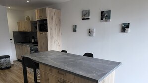 A modern kitchen with wooden cabinets, a black countertop, and a dining area with a table and chairs. - SEASONAL RENTAL RENOVATED STUDIO 35M2 IN ORCIÈRES (ORCIÈRES)