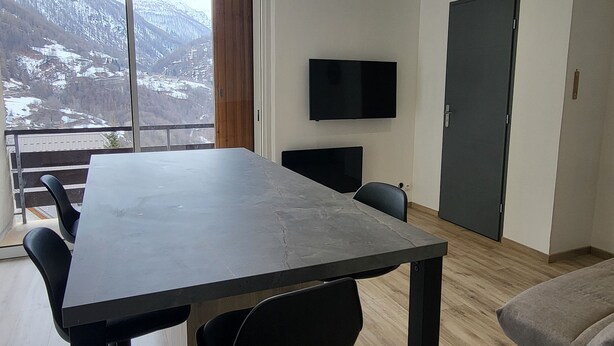 A modern room with a large table, two chairs, a TV, and a door. - SEASONAL RENTAL RENOVATED STUDIO 35M2 IN ORCIÈRES (ORCIÈRES)