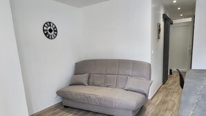 A modern living room with a beige sofa, a clock on the wall, and a wooden floor. - SEASONAL RENTAL RENOVATED STUDIO 35M2 IN ORCIÈRES (ORCIÈRES)