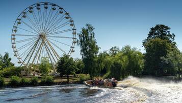 A river with a boat carrying passengers, a large Ferris wheel, and trees in the background.