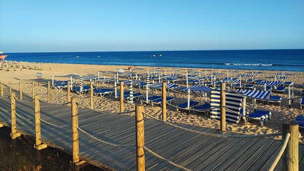 Une plage bordée de rangées de chaises de plage et de parasols à rayures bleues et blanches, de promenades en bois et, au loin, l’océan.