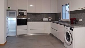 Une cuisine moderne avec des meubles blancs, un four encastré, un micro-ondes, un grille-pain et un lave-linge.