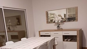 Un coin repas avec une table dressée pour quatre personnes, un meuble en bois avec des tiroirs et un grand miroir au-dessus du meuble.