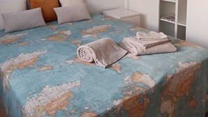 Une chambre à coucher avec un lit, des oreillers, une armoire et une couvre-lit décorée de motifs de cartes géographiques.