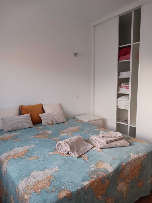 A bedroom with a bed, pillows, a wardrobe, and a map-themed bedspread.